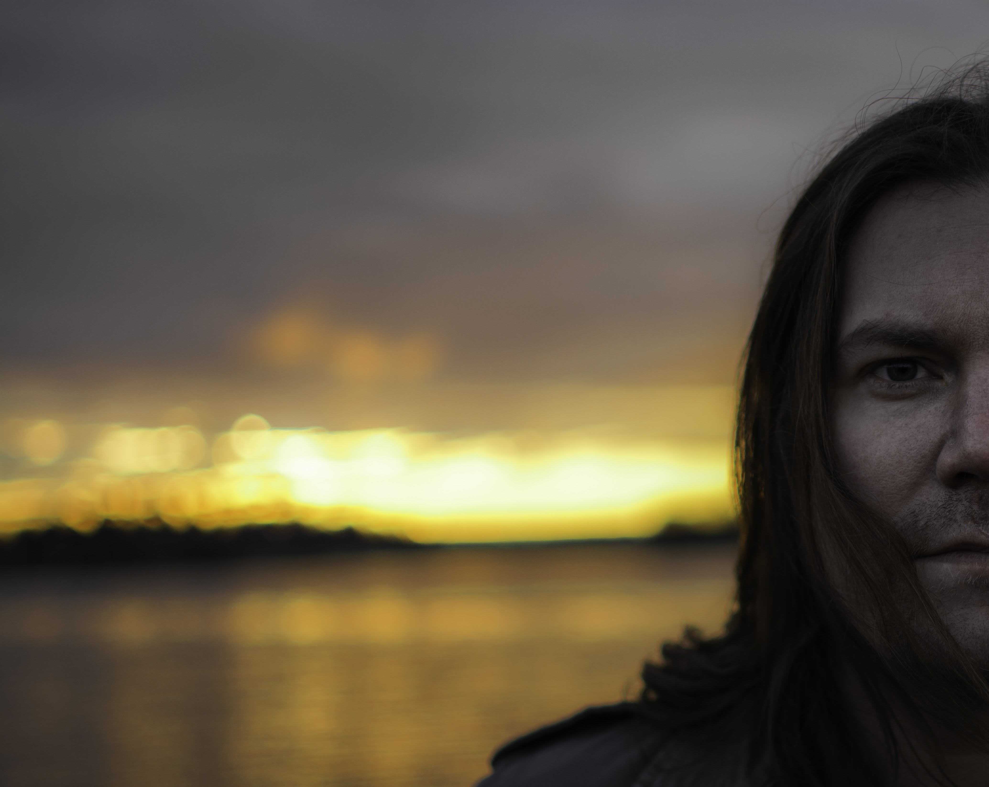 Man with long hair against golden sunset over water